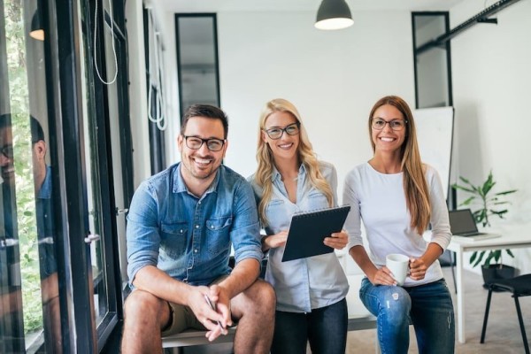 three young professionals smiling in an office width=