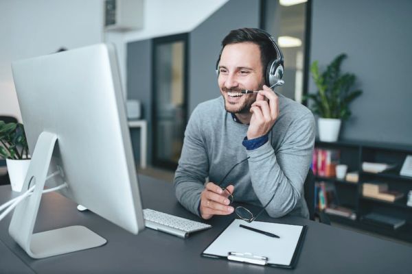 A smiling man wearing a headset sits at a computer